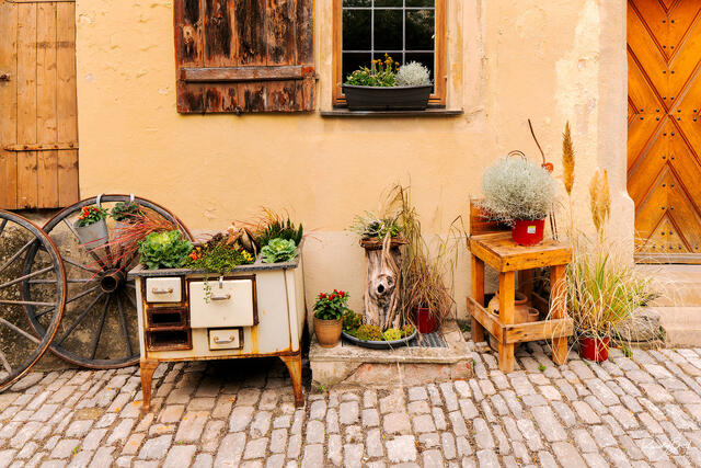 old wagon wheel and stove with flowers and plants next to house in Rothenburg Ob Der Tauber, Germany