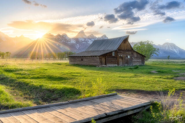 sunset over TA Moulton barn in the Grand Teton National Park with s sunburst casting lights rays through the scene.
