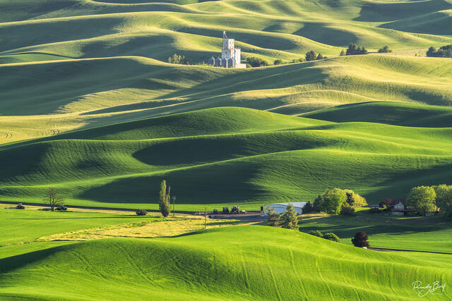 gold light washes over the hills of the Palouse at sunset overlooking the granary and small tractors from Steptoe Butte.