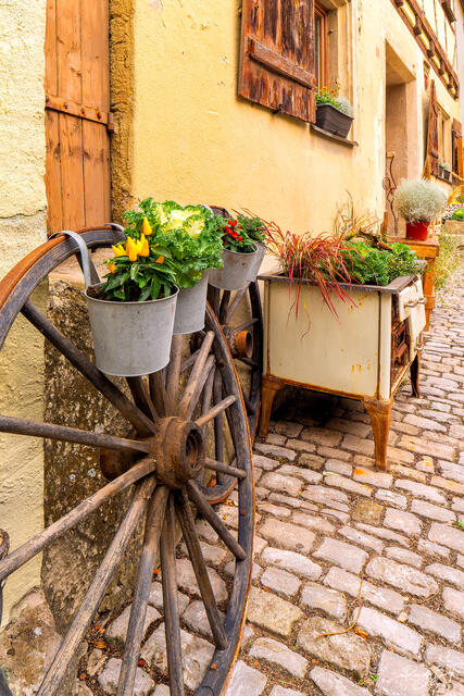 wagon wheel and old stove next to a house in Rothenburg Ob Der Tauber with plants and flowers