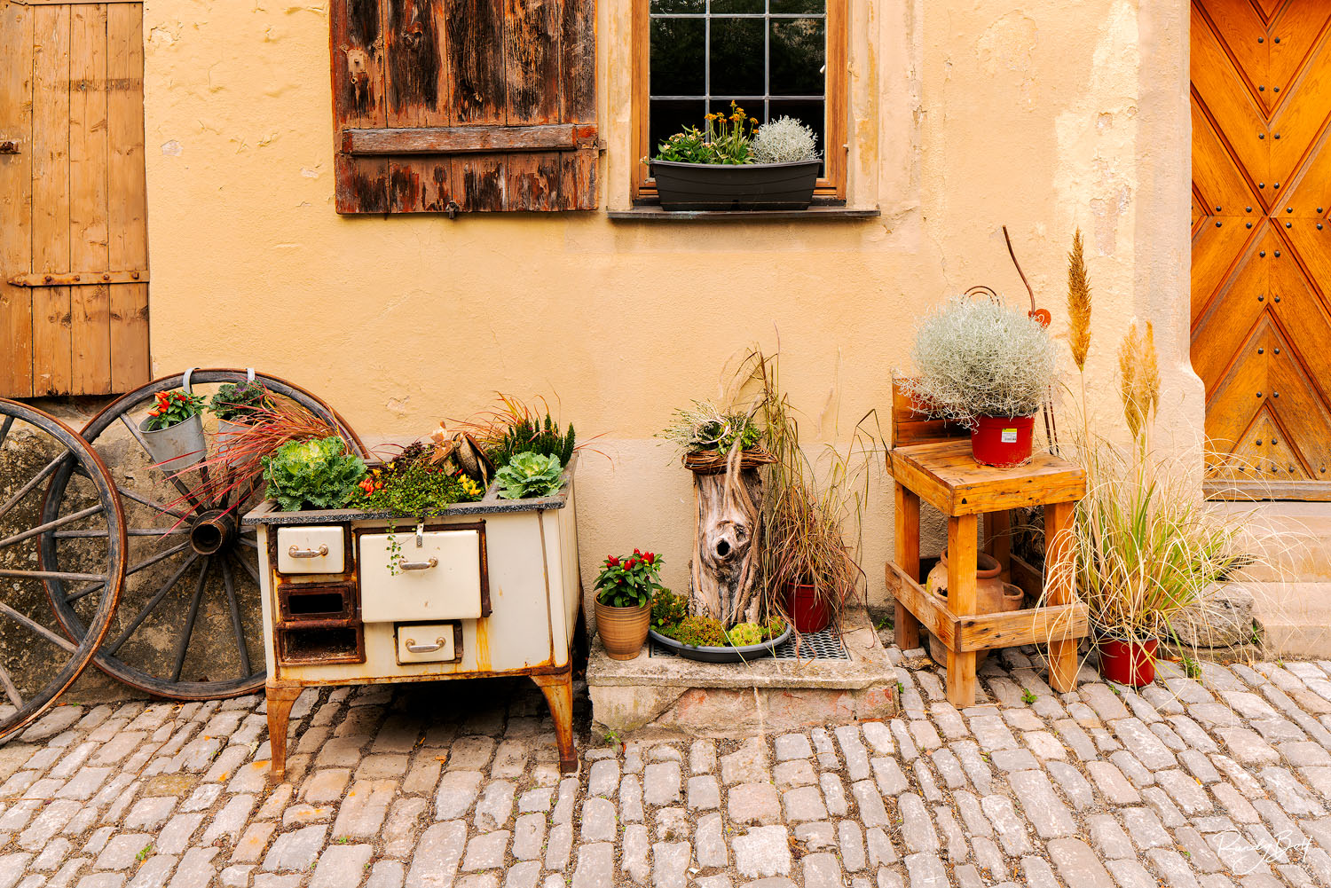 old wagon wheel and stove with flowers and plants next to house in Rothenburg Ob Der Tauber, Germany