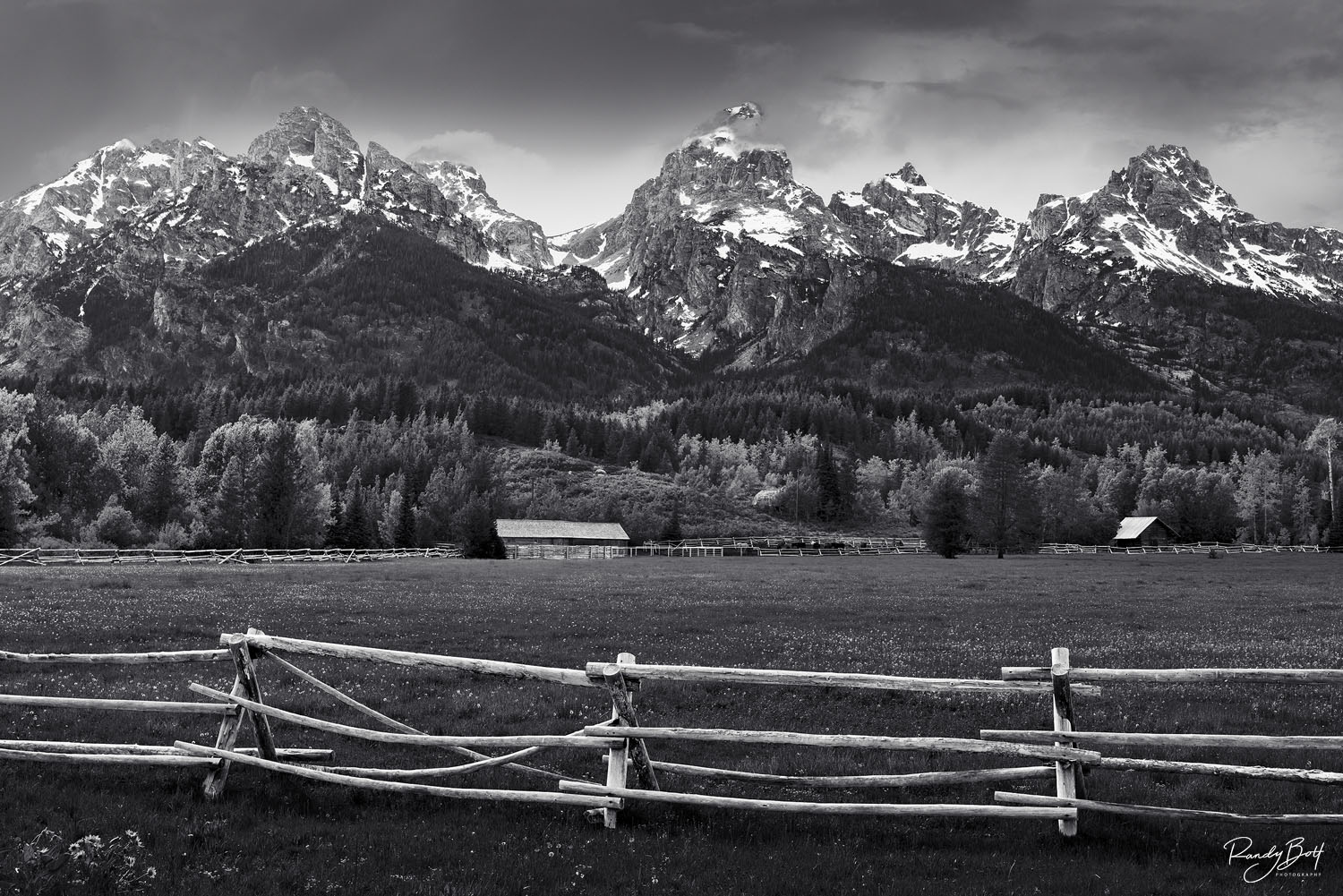 Black and white photo of the grand Teton mountains with fences and barns